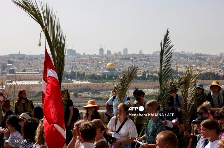 Umat Kristen dan anggota klerus mengambil bagian dalam prosesi tradisional Minggu Palma Katolik dari Bukit Zaitun ke Kota Tua Yerusalem, pada 10 April 2022, dengan pemandangan Masjid Kubah Batu di kompleks Masjid Al-Aqsha.